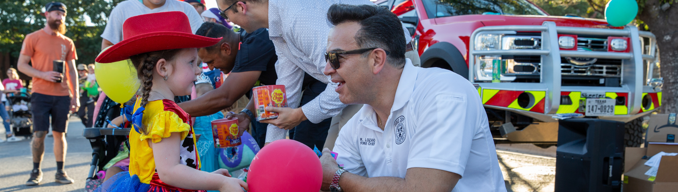 Fire Chief speaks with a child in costume at a community event near a fire truck
